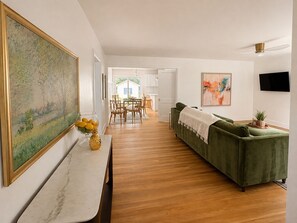 Ein Wohnzimmer mit einem grünen Sofa, einem Essbereich mit Tisch und Stühlen sowie einer Küche im Hintergrund.