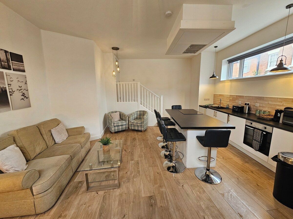 A modern living room with a sofa, chairs, a coffee table, and a kitchen area with a bar and seating.