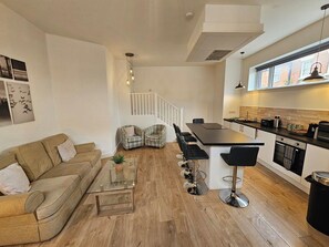 Una sala de estar moderna con un sofá, sillas, una mesa de centro y una zona de cocina con barra y asientos.
