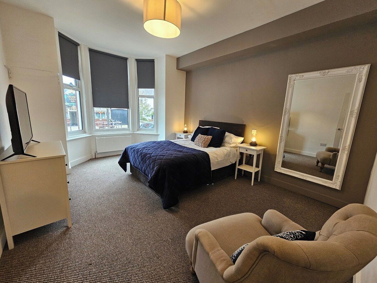 A hotel room with a bed, bedside tables, a chair, a TV, and a large mirror.