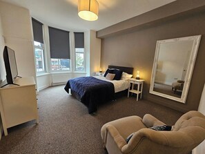 A hotel room with a bed, bedside tables, a chair, a TV, and a large mirror. - Kings Central 3 Bedroom - Free Parking & wifi (Southport)