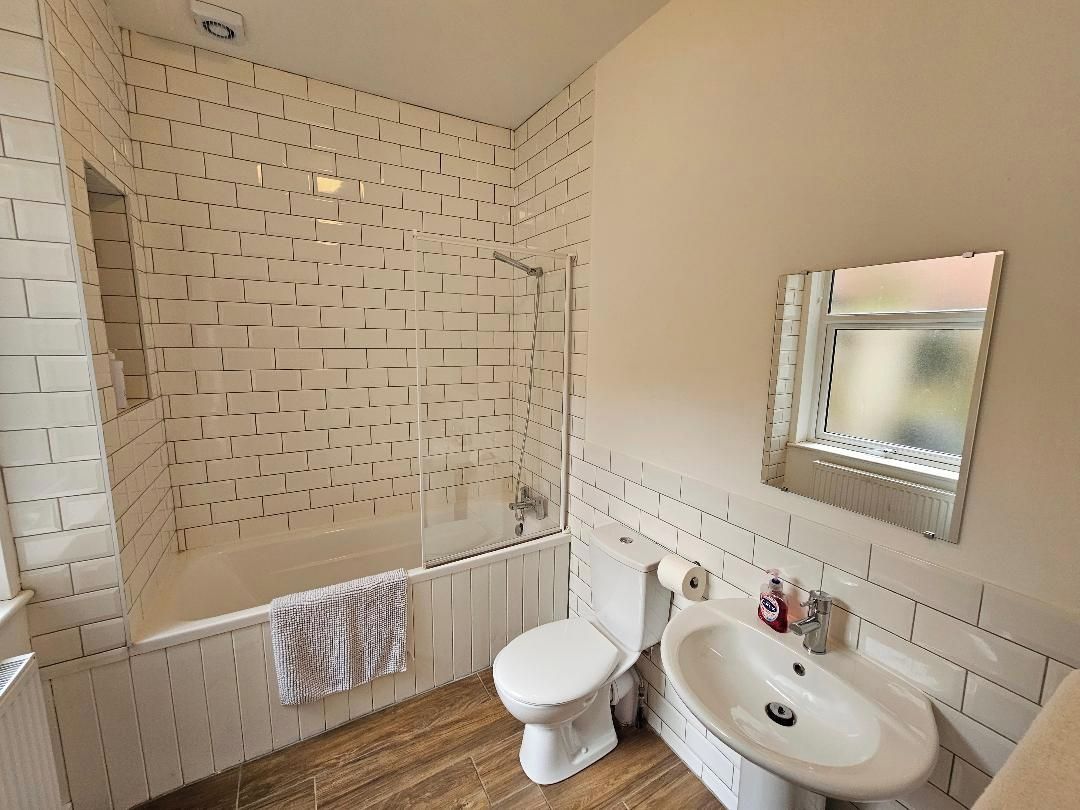 A bathroom with a white tiled shower, a toilet, and a sink.