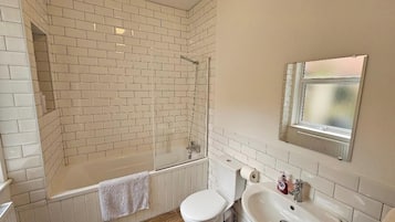 A bathroom with a white tiled shower, a toilet, and a sink.