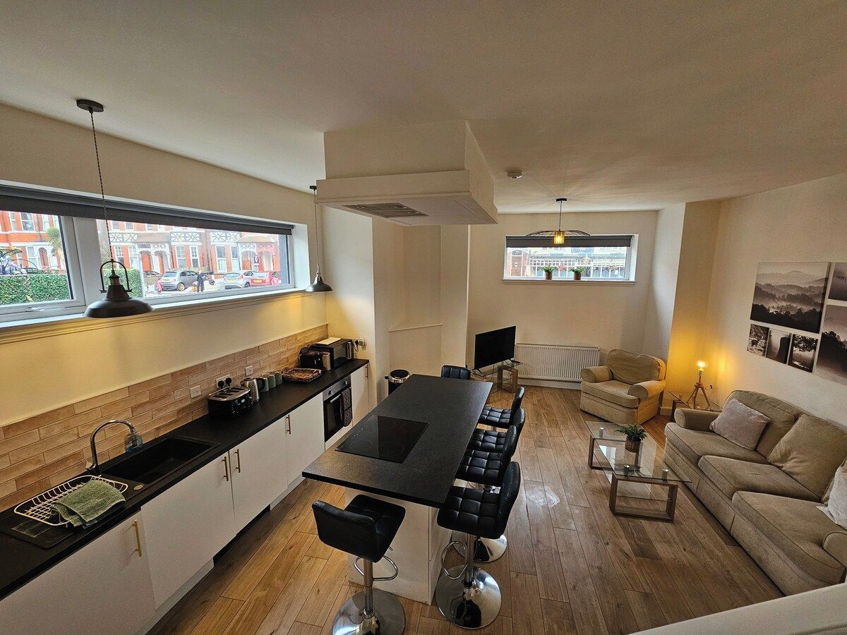 A modern kitchen with a central island, dining area with chairs, a sofa, and a TV.