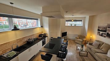 A modern kitchen with a central island, dining area with chairs, a sofa, and a TV.
