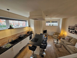 A modern kitchen with a central island, dining area with chairs, a sofa, and a TV. - Kings Central 3 Bedroom - Free Parking & wifi (Southport)