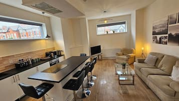 A modern kitchen with a central island, bar stools, and a dining area with a sofa and coffee table.