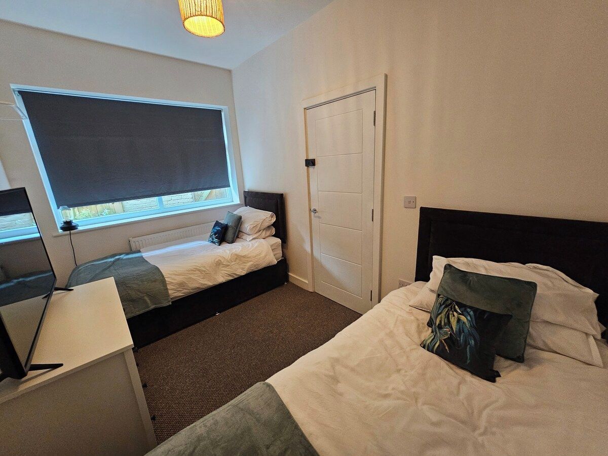 A hotel room with two beds, a desk, a chair, a window with a view, and a door.