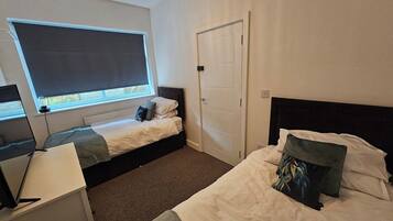 A hotel room with two beds, a desk, a chair, a window with a view, and a door.