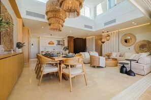 A spacious living area with a high ceiling, a dining table set for six, and a modern kitchen in the background. - Luxury 3-Bedroom Villa with Private Pool & Jacuzzi (Barú)