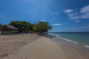 Ein Strand mit einer strohgedeckten Hütte, Liegestühlen und einem ruhigen Meer.