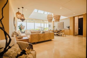 A modern living room with a sofa, a dining area with a table and chairs, and a kitchen area with a counter and cabinets. - Luxury 3-Bedroom Villa with Private Pool & Jacuzzi (Barú)