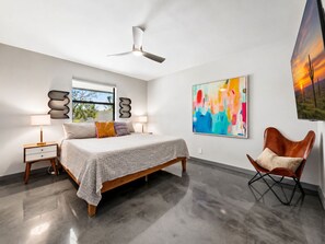 Ein Schlafzimmer mit einem Bett, Nachttischlampen, einem Deckenventilator, einem Fenster und einem großen abstrakten Gemälde.