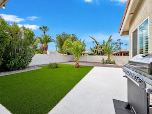 A backyard with artificial grass, a barbecue grill, and various plants including palm trees. - Beech Creek Sun Lakes (Chandler)