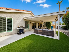 Un patio techado al aire libre con una parrilla, zona de estar y vista de la casa.