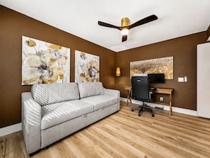 A modern living room with a grey sofa, wooden flooring, a ceiling fan, and artwork on the walls. - Beech Creek Sun Lakes (Chandler)