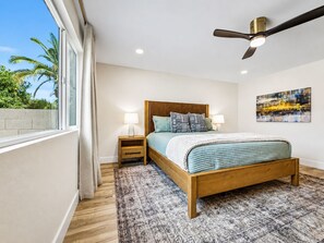 A bedroom with a wooden bed, two bedside tables with lamps, a ceiling fan, a large window with curtains, and a painting on the wall. - Beech Creek Sun Lakes (Chandler)