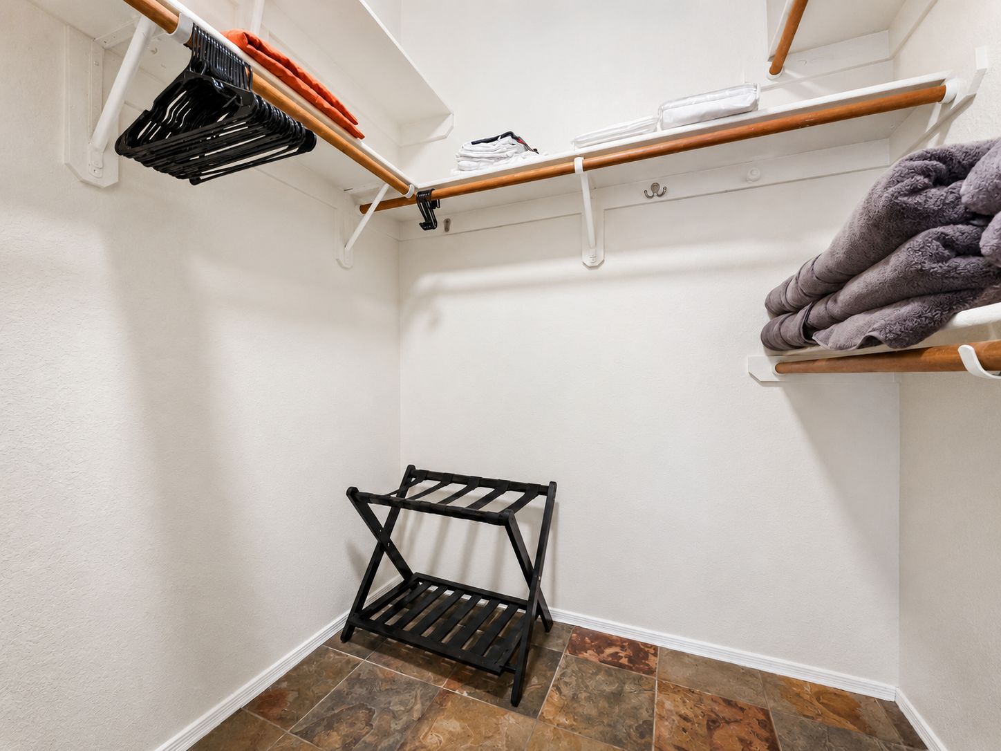 A corner of a room with a black metal drying rack, a white wall, and a tiled floor.