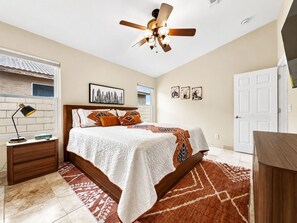 A bedroom with a bed, a nightstand, a desk, a ceiling fan, and a door. - Amazing Views for Miles! Oro Valley Stunner (Oro Valley)