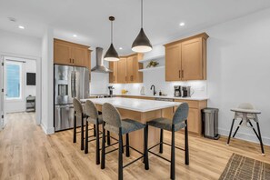 Een moderne keuken met roestvrijstalen apparatuur, houten kastjes en een centraal eiland met barkrukken.