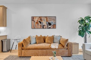 Ein Wohnzimmer mit einem beigen Sofa, einem Gemälde, einer Topfpflanze und einem Mülleimer.