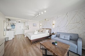 Una habitación de hotel moderna con cama, sofá, mesa de centro y kitchenette.