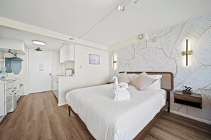 A hotel room with a bed, a bedside table, a wall-mounted light, and a view of the bathroom. - 36FL New Cozy Apartment Great View Central Waikiki (Honolulu)