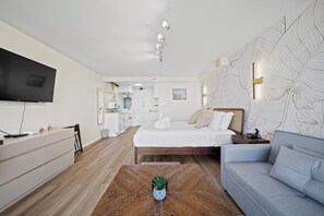 Quarto de hotel moderno com cama, sofá, televisão de tela plana e área de refeições.