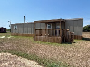 A single-story building with a wooden deck and a small porch. - 2-bedroom, 1 bath house in Palacios with Pool, Boat ramp, fishing pier and bar (Palacios)