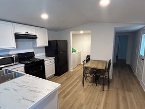 A compact kitchen with white cabinets, a black refrigerator, a microwave, and a stove. There's a wooden dining table with chairs. - 2-bedroom, 1 bath house in Palacios with Pool, Boat ramp, fishing pier and bar (Palacios)