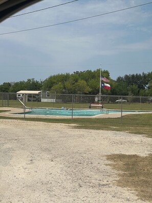 Ein Swimmingpool mit Fahnenmast, umzäunt und von Bäumen gesäumt.
