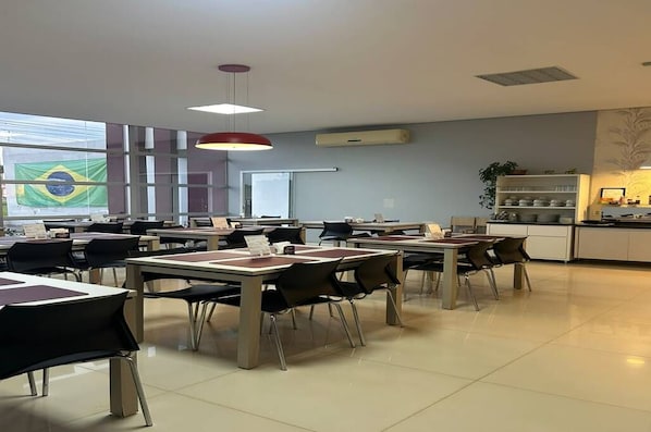 A dining area with tables and chairs, a kitchen area with shelves, and a large window with a flag.