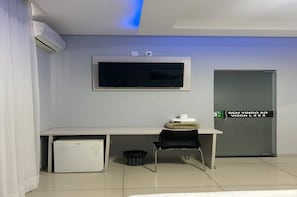 A room with a bed, a desk with a computer, a chair, a TV, and a door with a sign.