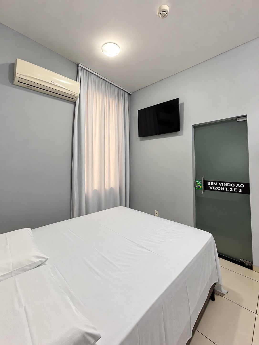 Ein Hotelzimmer mit einem Bett, einem Flachbildfernseher, einer Klimaanlage, einer Schiebetür und einem Schild mit einer Flagge.