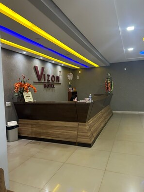 A reception desk with a sign for Vizon Hotel, a trash bin, and a decorative item on the wall.