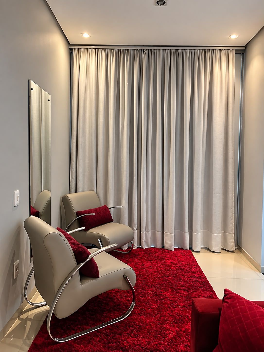 A modern room with a large mirror, two chairs with red cushions, a red carpet, and a large window with curtains.