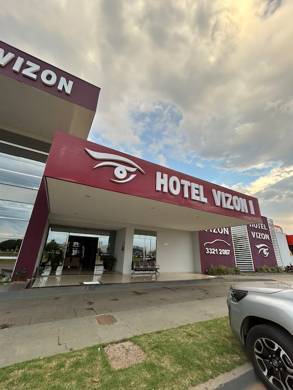 A hotel named 'Hotel Vizon' with a modern facade, a prominent eye logo, and a contact number.