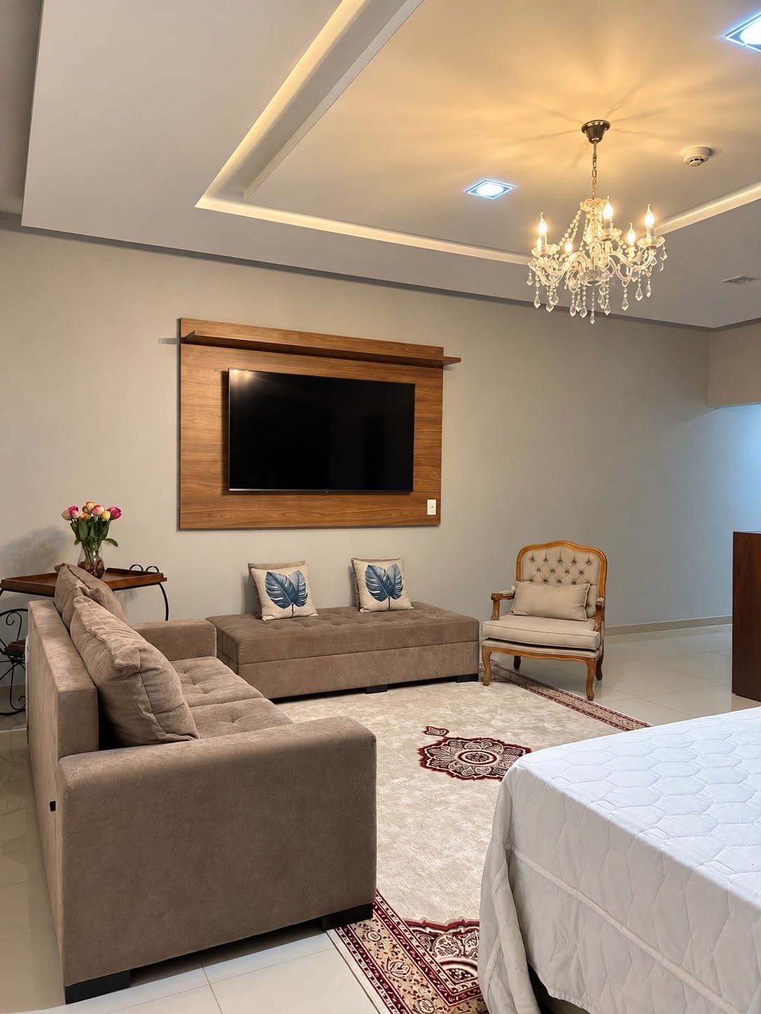 A modern living room with a flat-screen TV, a sofa, a chair, and a chandelier.