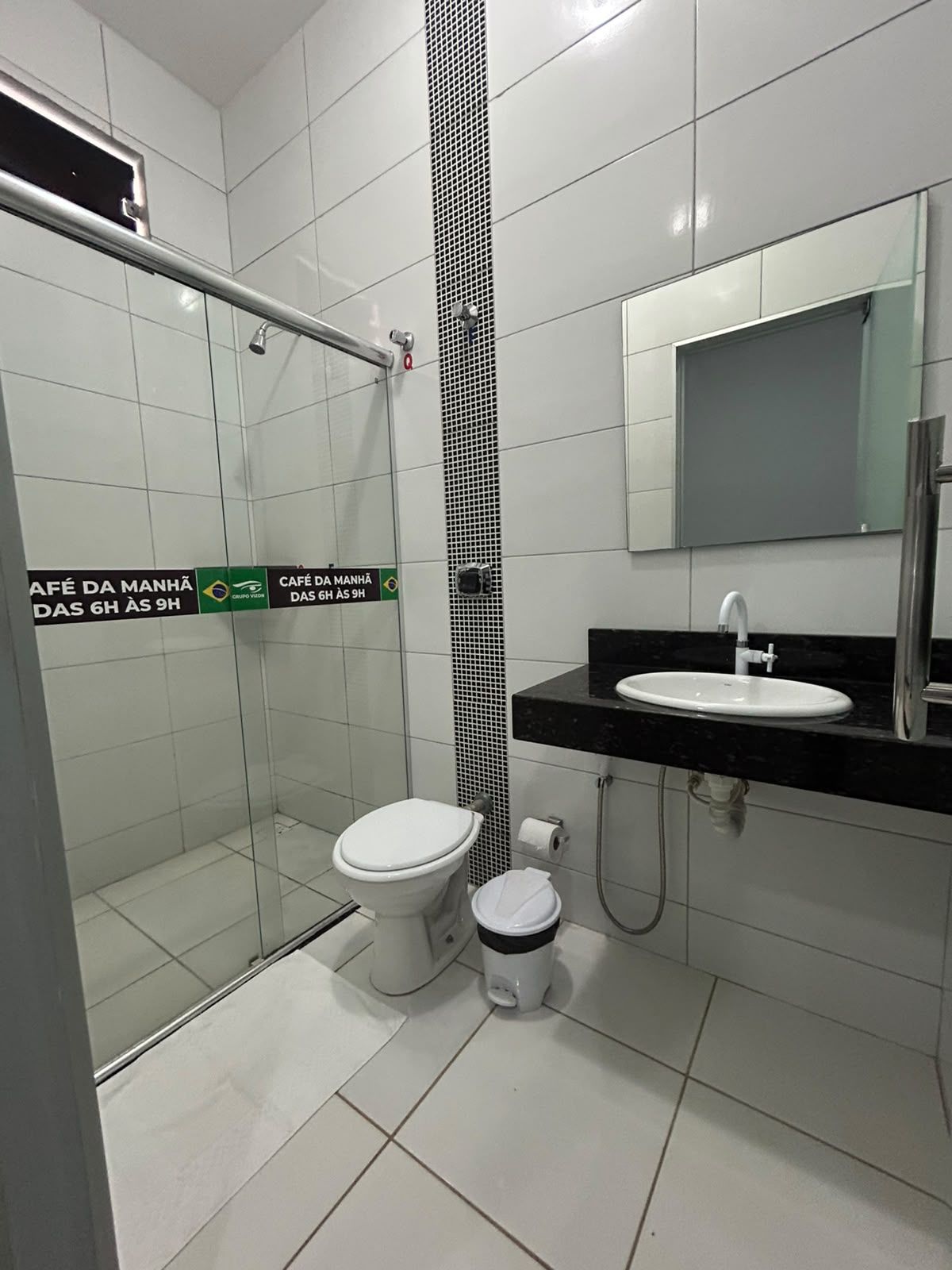 Ein modernes Badezimmer mit einer Duschkabine aus Glas, einer weißen Toilette, einem schwarzen Waschbecken mit Spiegel darüber und einem Mülleimer.