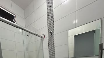 Ein modernes Badezimmer mit einer Duschkabine aus Glas, einer weißen Toilette, einem schwarzen Waschbecken mit Spiegel darüber und einem Mülleimer.