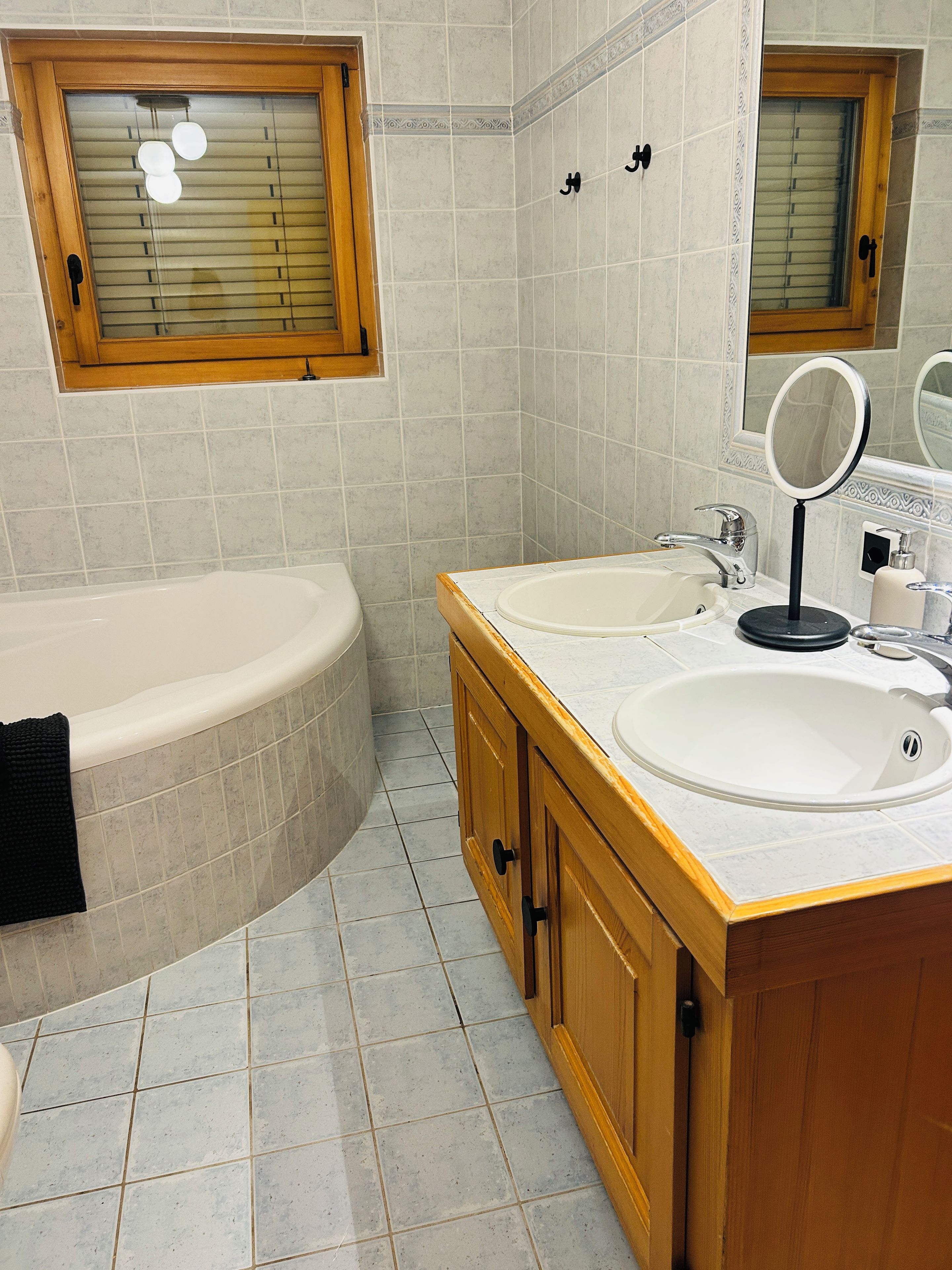 A bathroom with a bathtub, two sinks, a vanity with a mirror, and tiled walls.