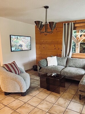 A living room with a sofa, a chair, a coffee table, a painting on the wall, and a wooden wall. - Spacious 3-bed, 3-bath flat in the centre of Verbier. Pet-friendly! (Val de Bagnes)