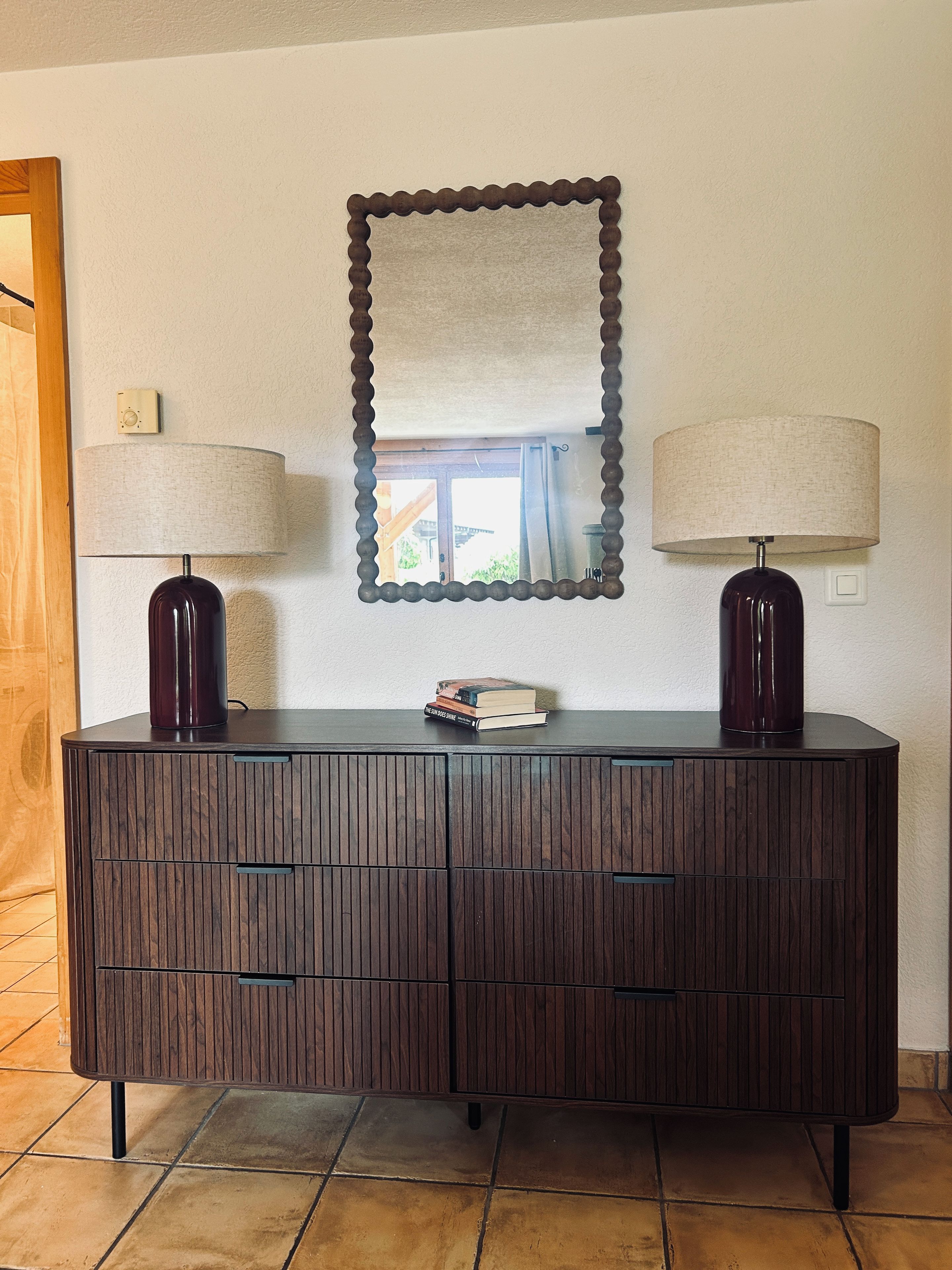 A dark wooden cabinet with two lamps, a mirror, and a small stack of books.