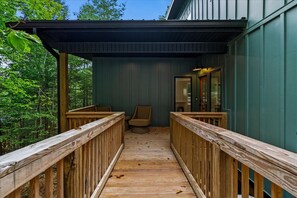 Um deck de madeira com área coberta, uma cadeira e uma porta que dá para o interior.