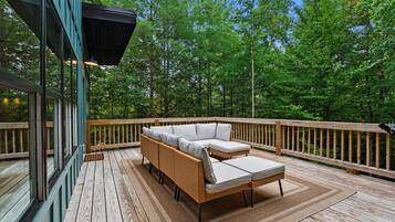 A wooden deck with a wicker sofa and a small table, surrounded by a wooden railing.