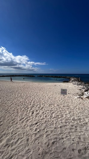 A sandy beach with a clear sky and a rocky shoreline. - Sunset Cove Condo 314 Beach View Bliss-2-Bedroom (George Town)