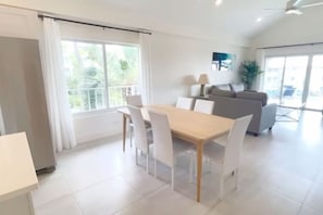 Ein modernes Wohnzimmer mit Essbereich, großen Fenstern und einem grauen Sofa.