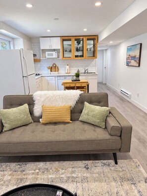 A modern kitchen with white cabinets, a microwave, and a wooden dining table. - Cozy Langford Suite (Victoria)