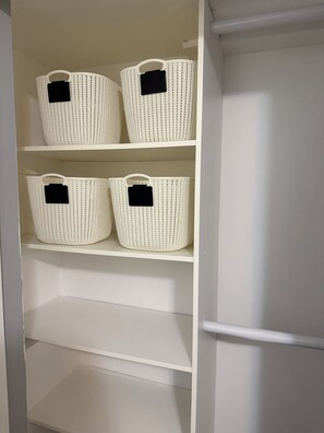 A white shelving unit with four woven baskets, each with a black handle and a black label. - Cozy Langford Suite (Victoria)