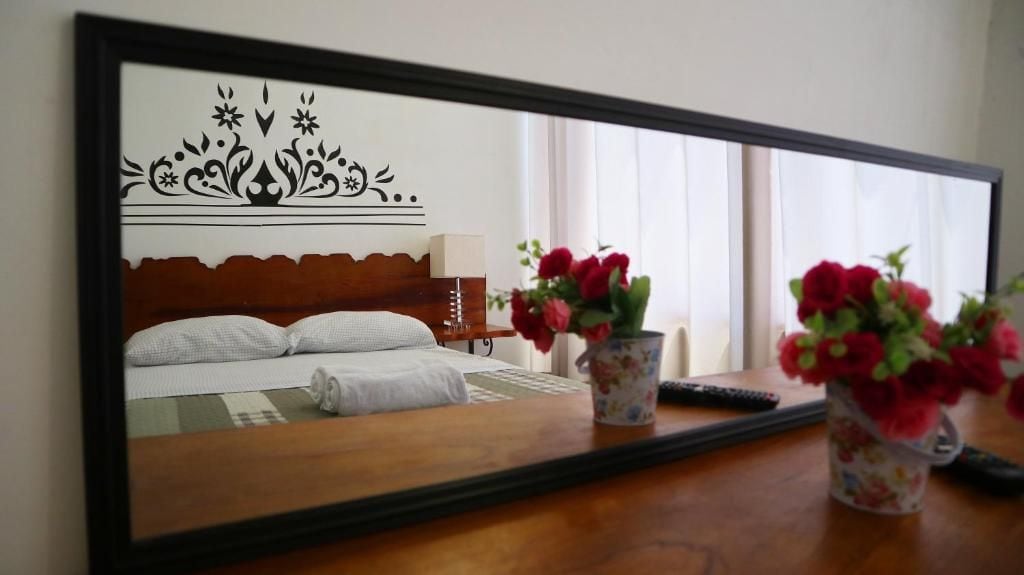Een hotelkamer met een bed, nachtkastje, lamp en een spiegel die de kamer weerkaatst.